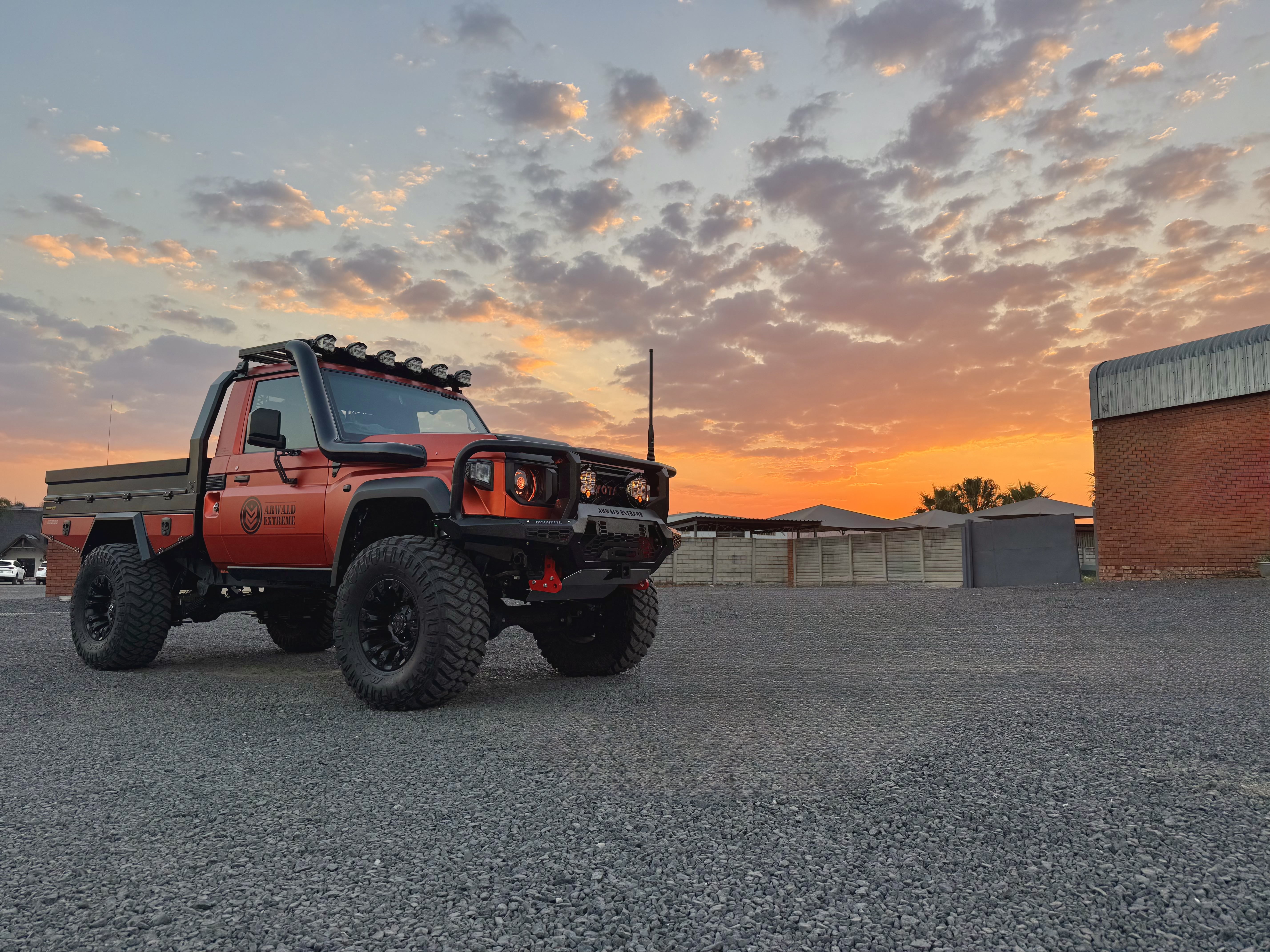 Red Land Cruiser single-cab with roof lights at sunset